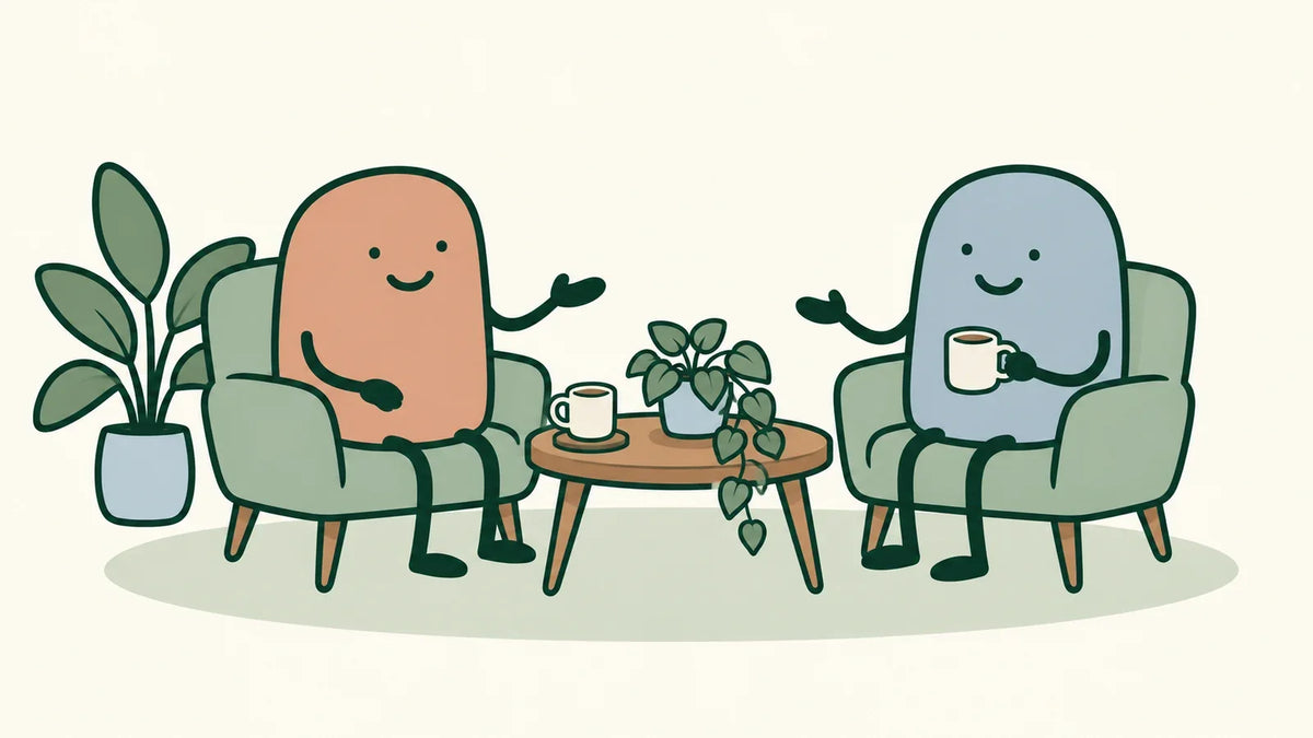 Two housemates talk across a small shared table, with cups and a plant between them.