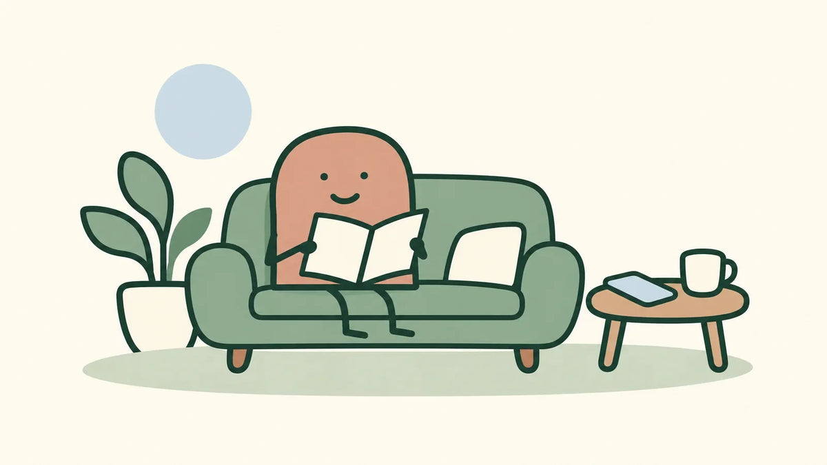 A terracotta character reads on a sage sofa while a phone and a cup rest on a nearby side table.